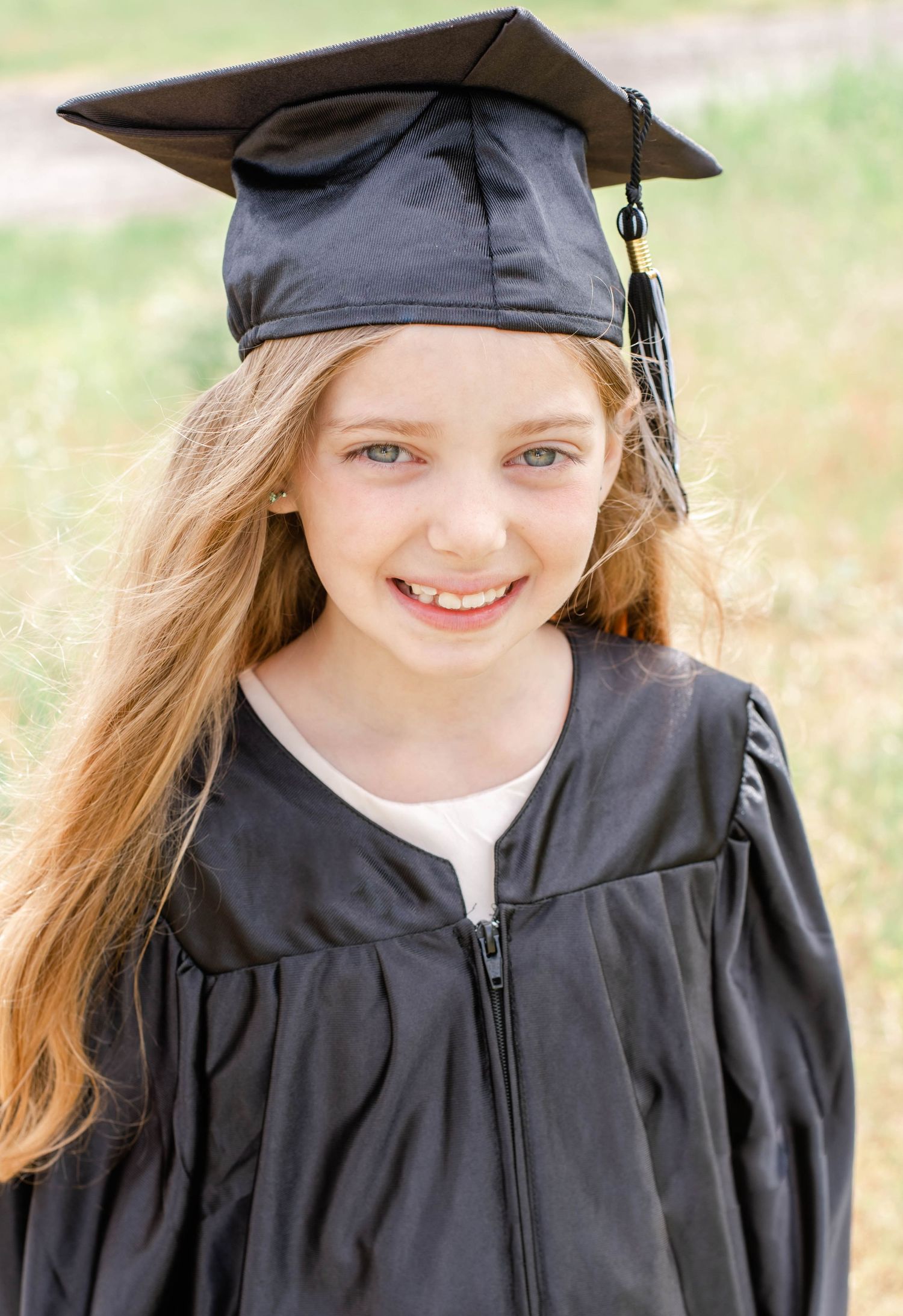 Graduate in black cap and gown smiles during outdoor graduation photo session.
