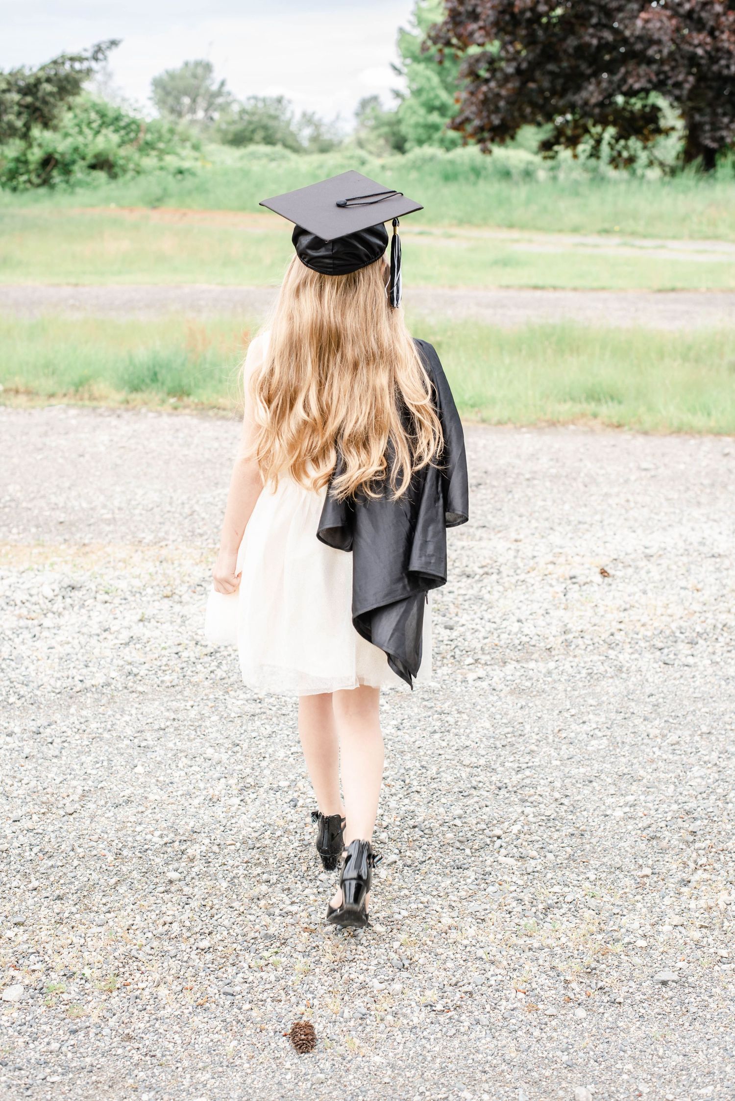 Graduate walks away on gravel path showing flowing movement of graduation gown.