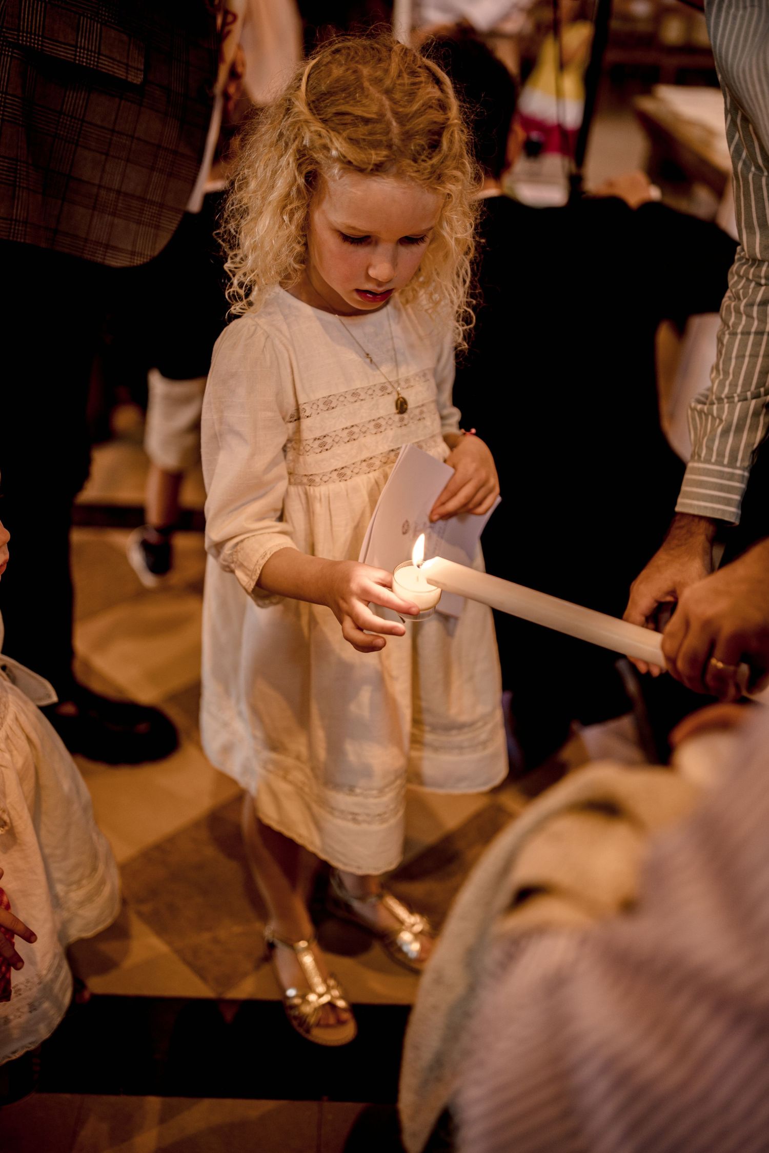 Child in white dress holding a candle during a ceremonial event.