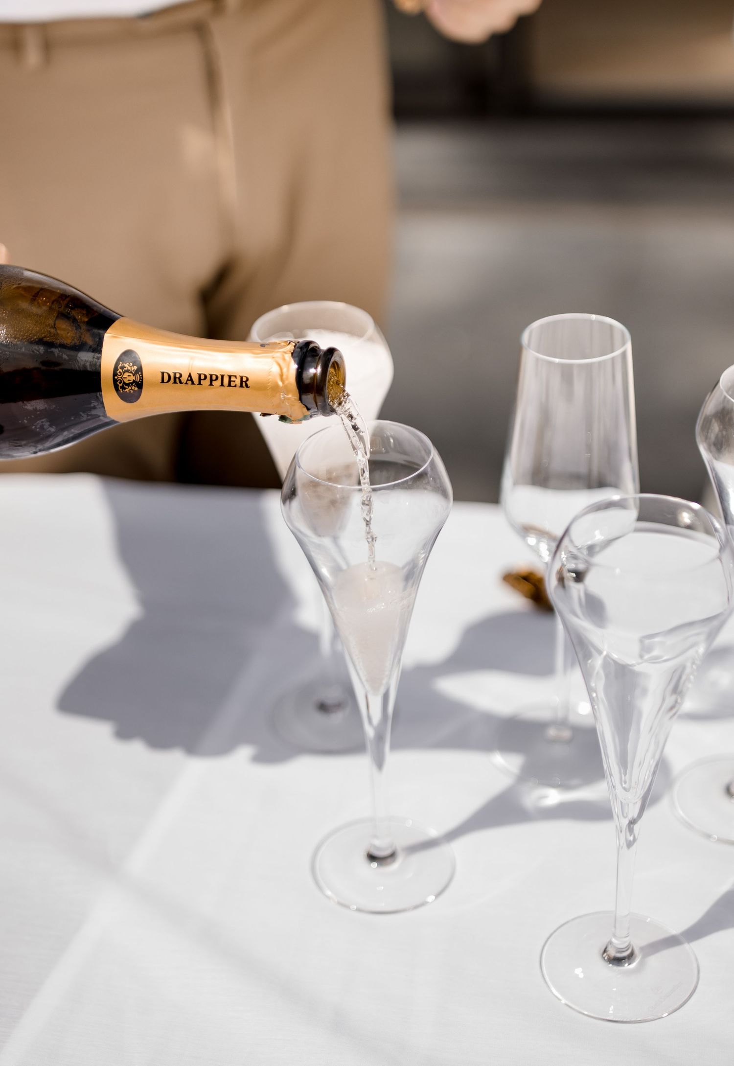 Drappier champagne being poured into elegant crystal flutes on a white tablecloth.