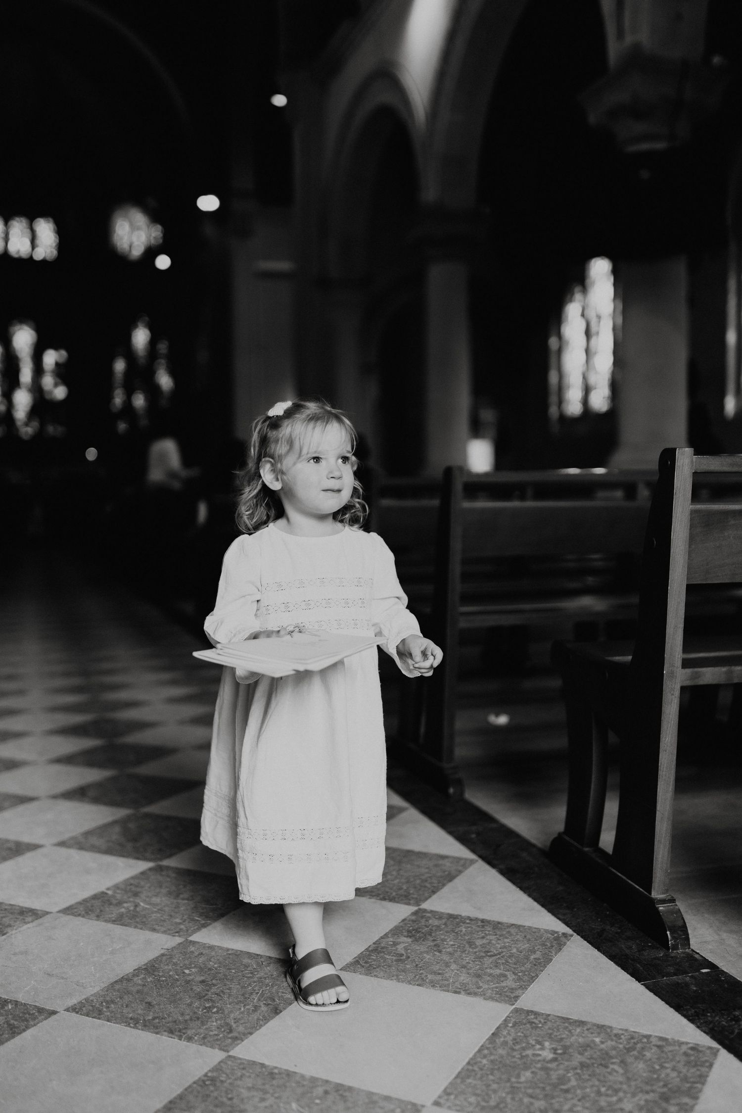 Young child in white dress standing on checkered floor inside a historic church.