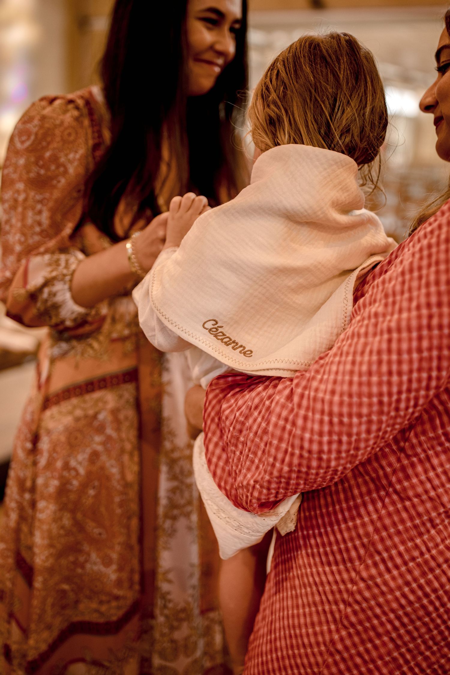 A baby in pink being held during a celebration with people in festive attire.