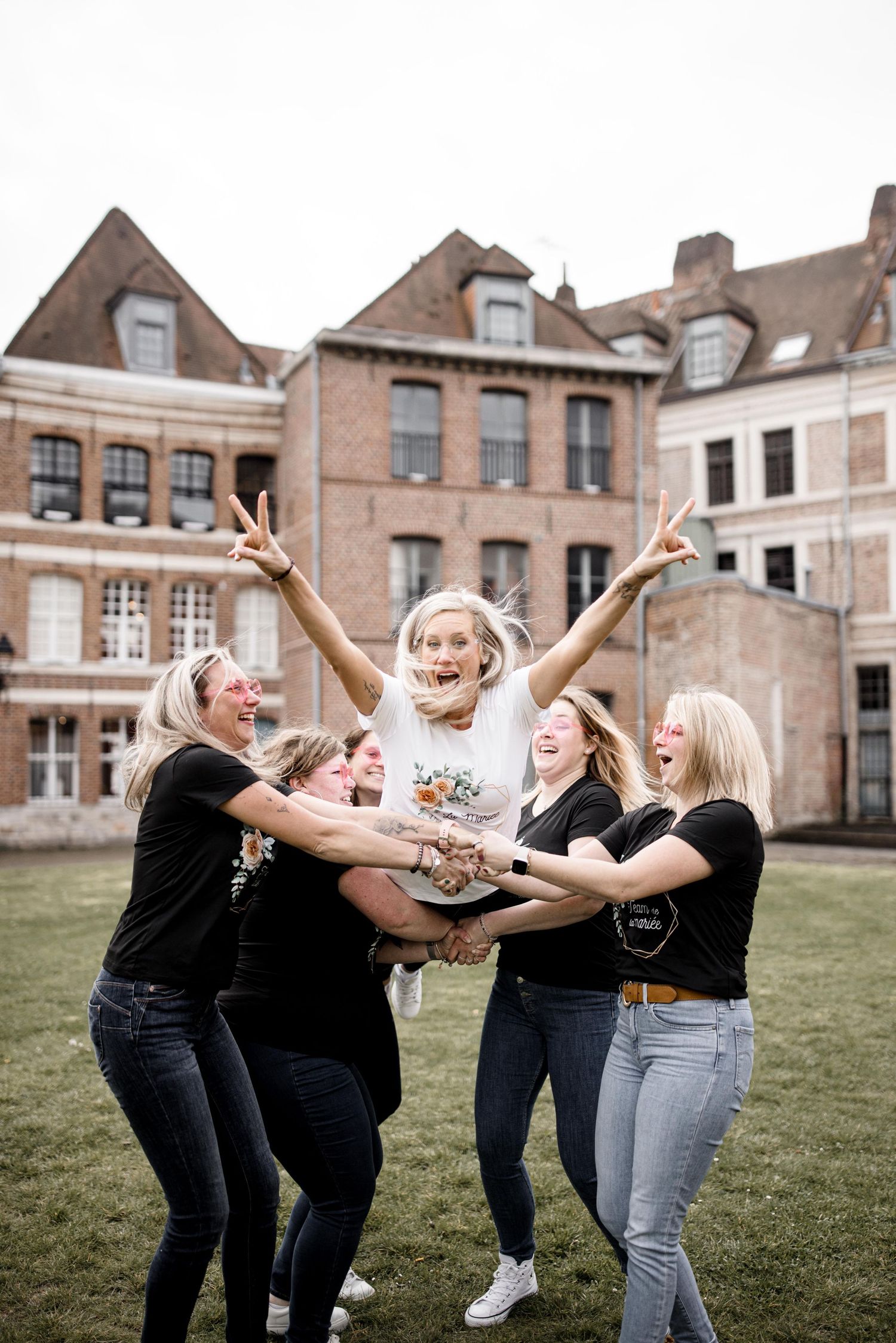 Friends lifting and celebrating together in front of a historic brick building.