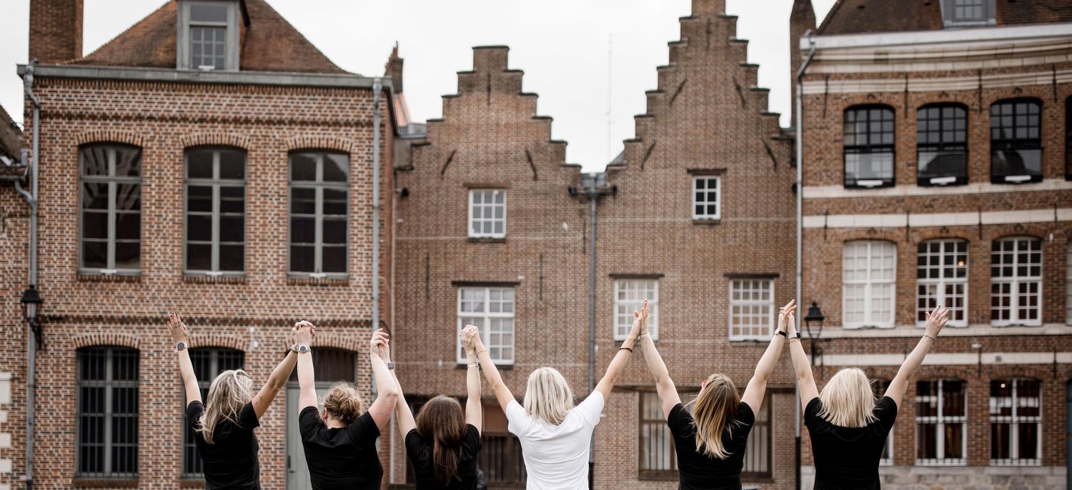 A group celebrating with raised hands in front of traditional Dutch stepped-gable buildings in Europe.