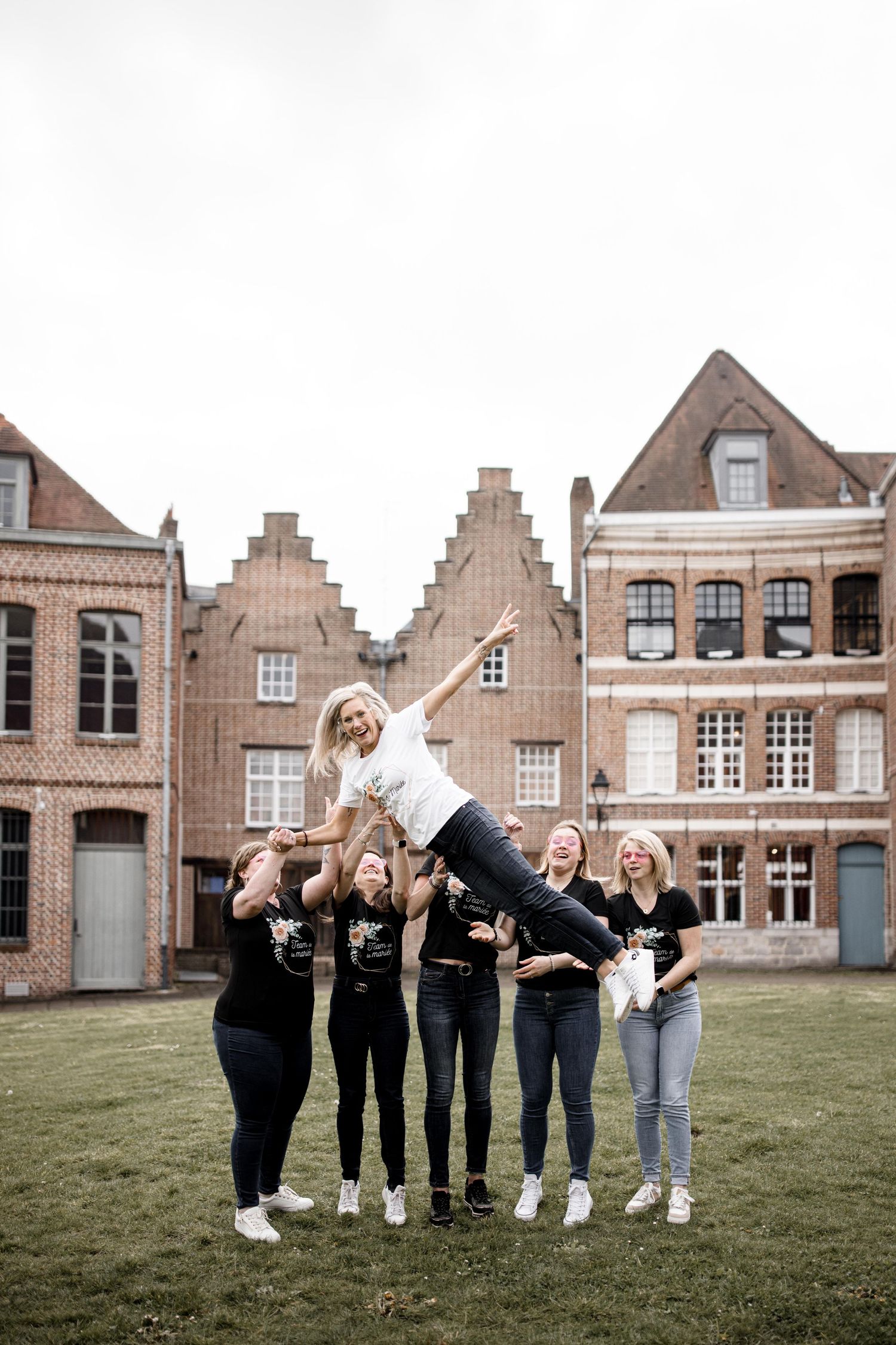 Friends performing a cheerful group stunt on grass in front of historic brick buildings.