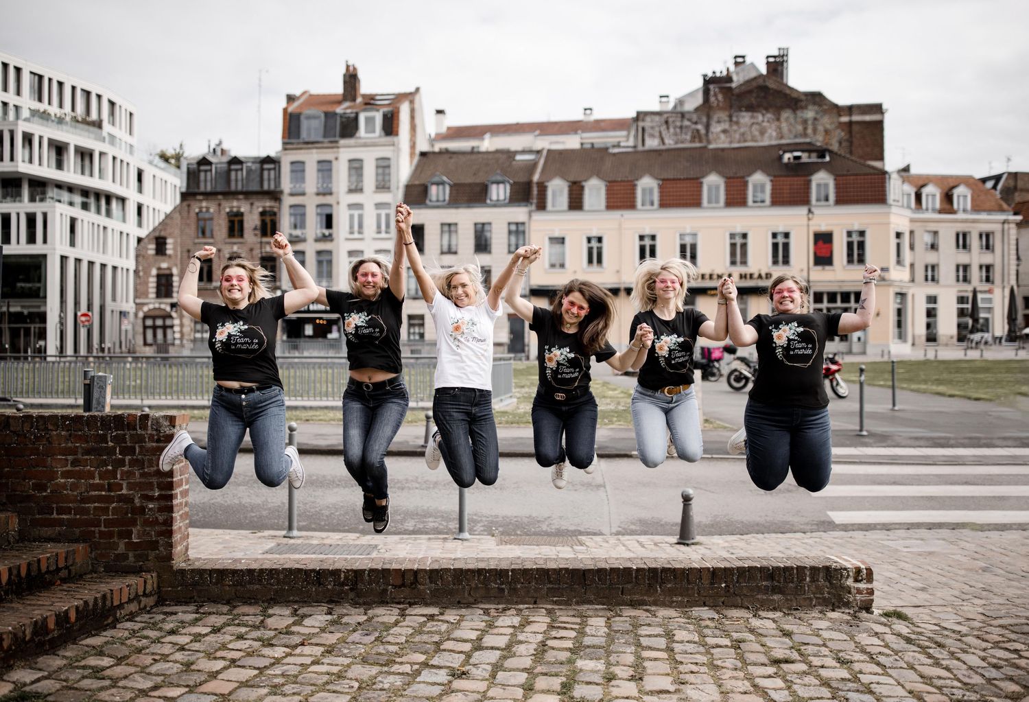 Group jumping simultaneously on cobblestone street with historic European buildings in background.