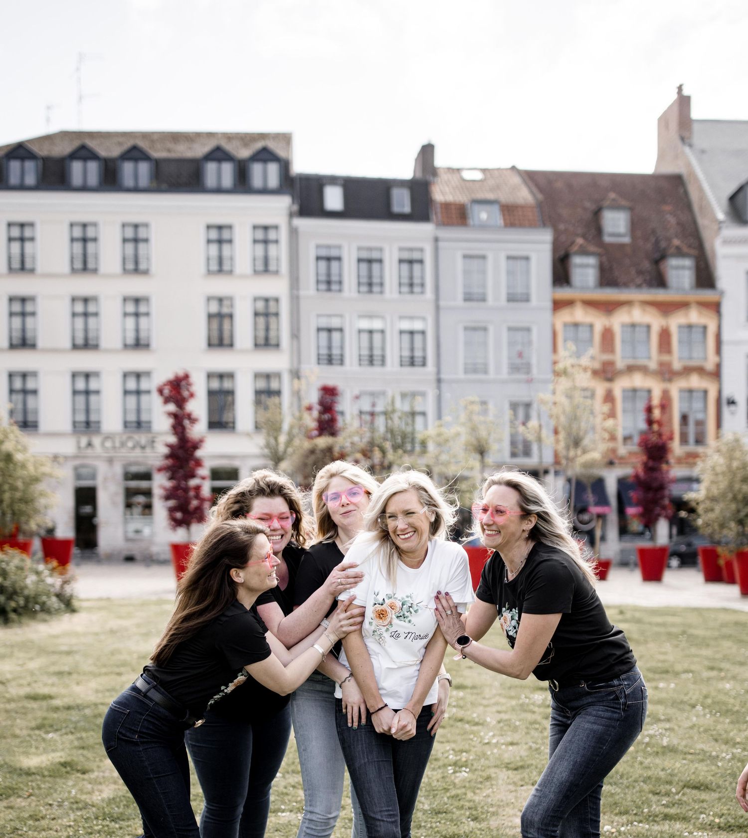 Friends sharing joyful moments on grassy area with European architecture in background.
