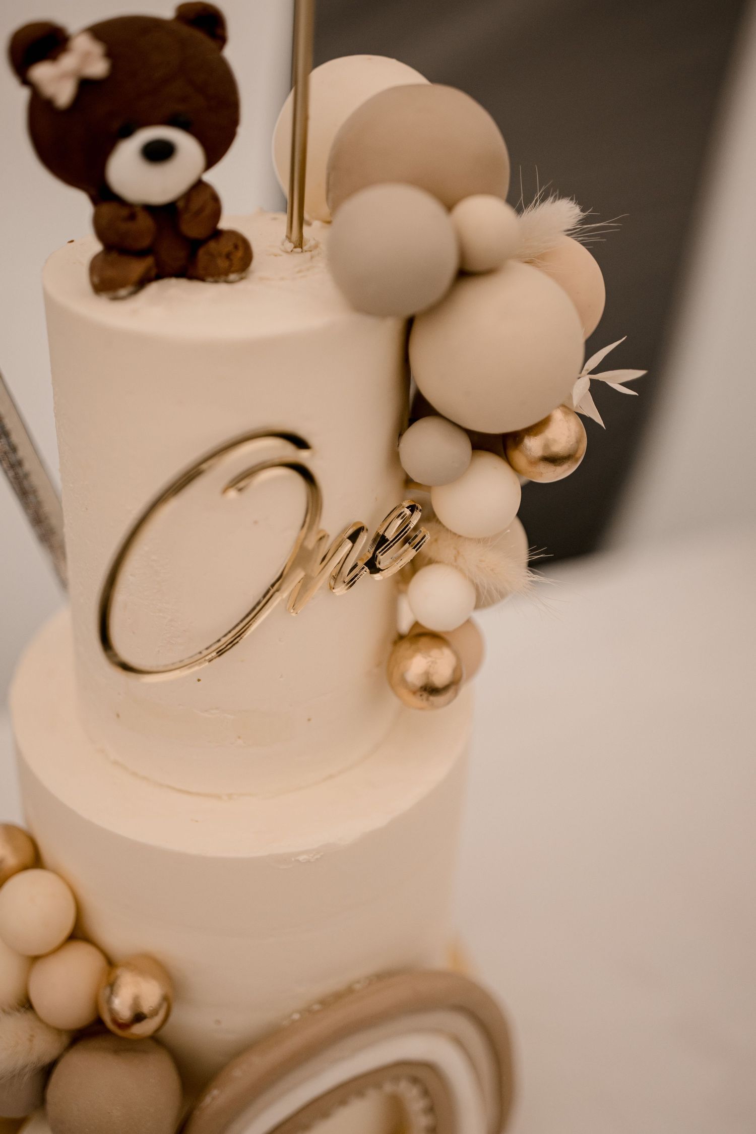 Gâteau blanc à plusieurs niveaux décoré d'un ours en peluche et d'une guirlande de ballons blush.