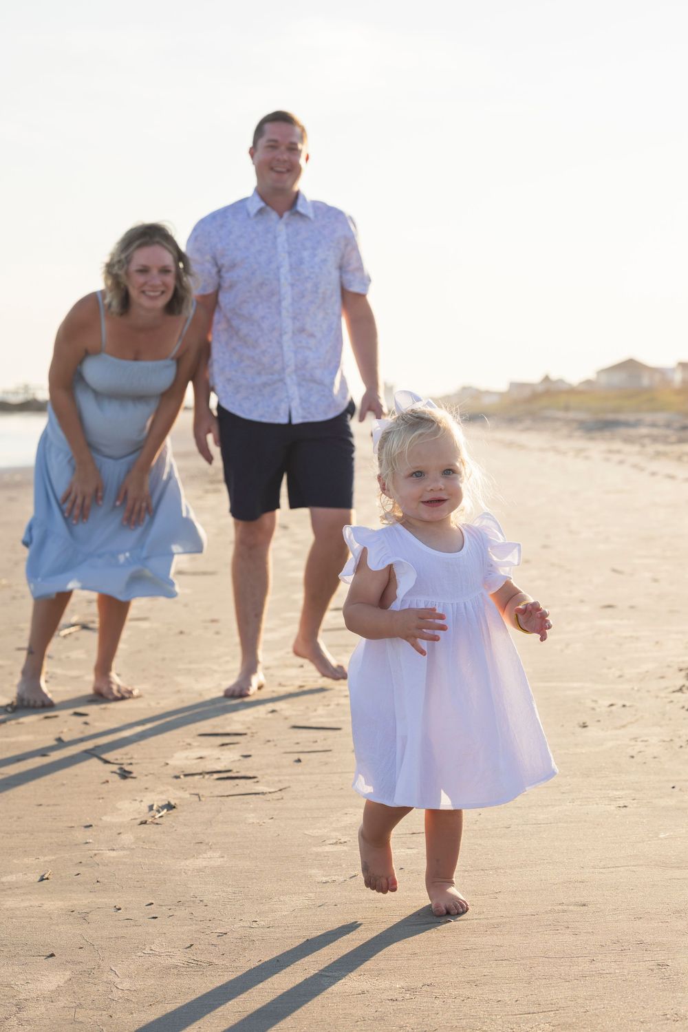A family walks and plays together on a sunny beach with long shadows cast on the sand.