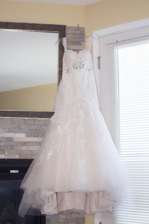 Elegant white lace mermaid wedding dress hanging on a hanger near a mirror and window in a bridal suite.