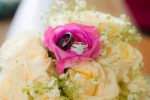 Wedding rings resting inside a pink rose on a bouquet of cream roses and baby's breath.