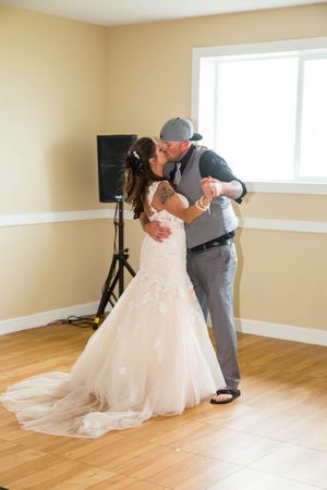 Bride and groom share a first dance kiss in white mermaid gown and gray suit at wedding reception.