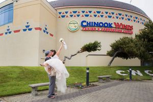 Groom lifting bride in wedding dress outside Chinook Winds Casino Resort on their wedding day.