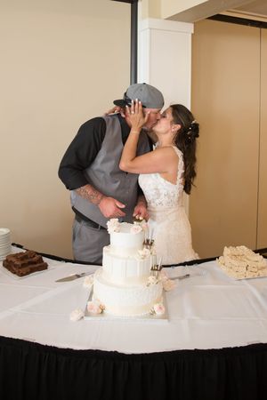 Bride and groom kiss while cutting their elegant four-tier white wedding cake at their reception.