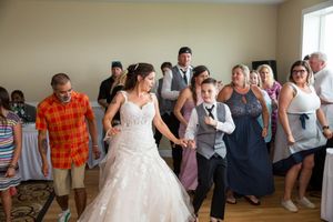Bride in white gown dances with guests at a wedding reception indoors, surrounded by smiling family and friends.