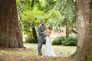 Bride and groom share a tender moment among towering trees in a lush forest setting during their outdoor wedding.