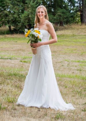 Bride in white strapless wedding gown holding yellow and white wildflower bouquet standing in a grassy field.