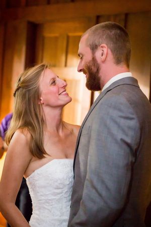 Bride in white strapless gown smiles up at bearded groom in gray suit during romantic wedding first dance.