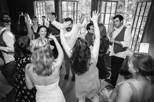 Black and white photo of wedding guests dancing joyfully at a lively indoor wedding reception celebration.