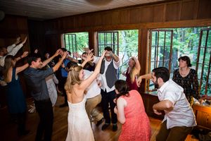 Bride and groom celebrate with cheering wedding guests raising hands in rustic woodland venue.