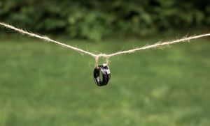 Black ceramic ring suspended from twine string outdoors with green grass background.