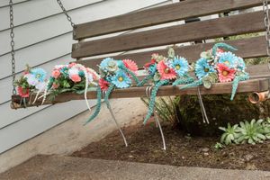 Colorful pink and blue floral bouquets with ribbons displayed on a wooden porch swing outdoors.