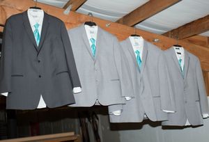 Four gray suits with teal ties on hangers displayed in a row, perfect for a wedding groomsmen ensemble.