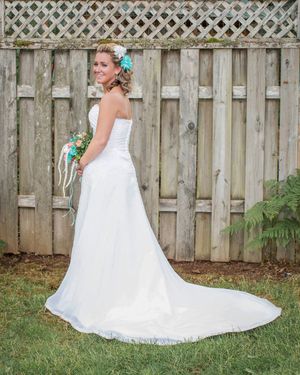 Bride in white strapless wedding gown with train, teal floral hair accessory, holding bouquet, posing by rustic wooden fence.