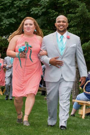 Bridesmaid in coral dress and groomsman in gray suit with teal tie walking down outdoor wedding aisle.