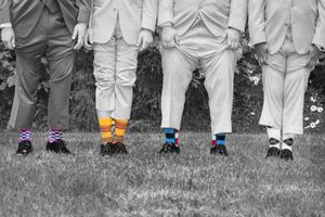 Groomsmen showing off colorful mismatched socks in a black and white wedding photo on green grass.