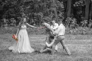 Playful black and white wedding photo showing couple in dramatic pose with attendant.