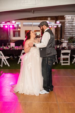Bride and groom share first dance on pink-lit dance floor at indoor wedding reception venue.