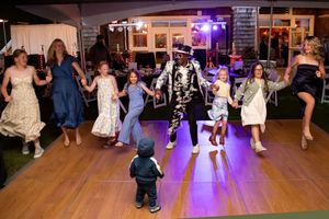Adults and children dancing joyfully on a lit dance floor at an outdoor evening wedding reception party.