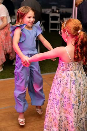 Two young girls in colorful dresses joyfully dancing together at a wedding reception on an outdoor dance floor.