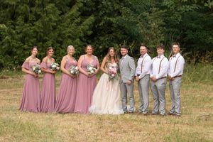 Wedding party posing outdoors with bridesmaids in mauve gowns and groomsmen in gray suits with suspenders.