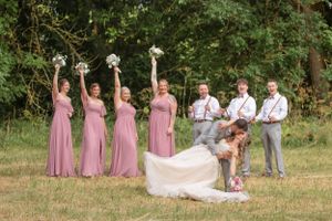 Fun wedding party photo with bridesmaids in pink dresses raising bouquets.