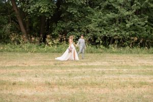 Couple walking together in a sunny field on their wedding day.