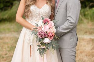 Close-up of bridal bouquet with pink roses and eucalyptus held against grey suit.