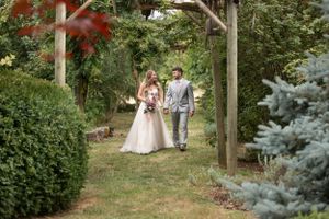 Couple strolling along garden path surrounded by evergreen trees and wooden posts.