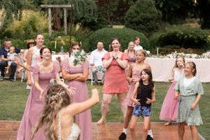 Wedding guests dance and celebrate on an outdoor patio in pink dresses.