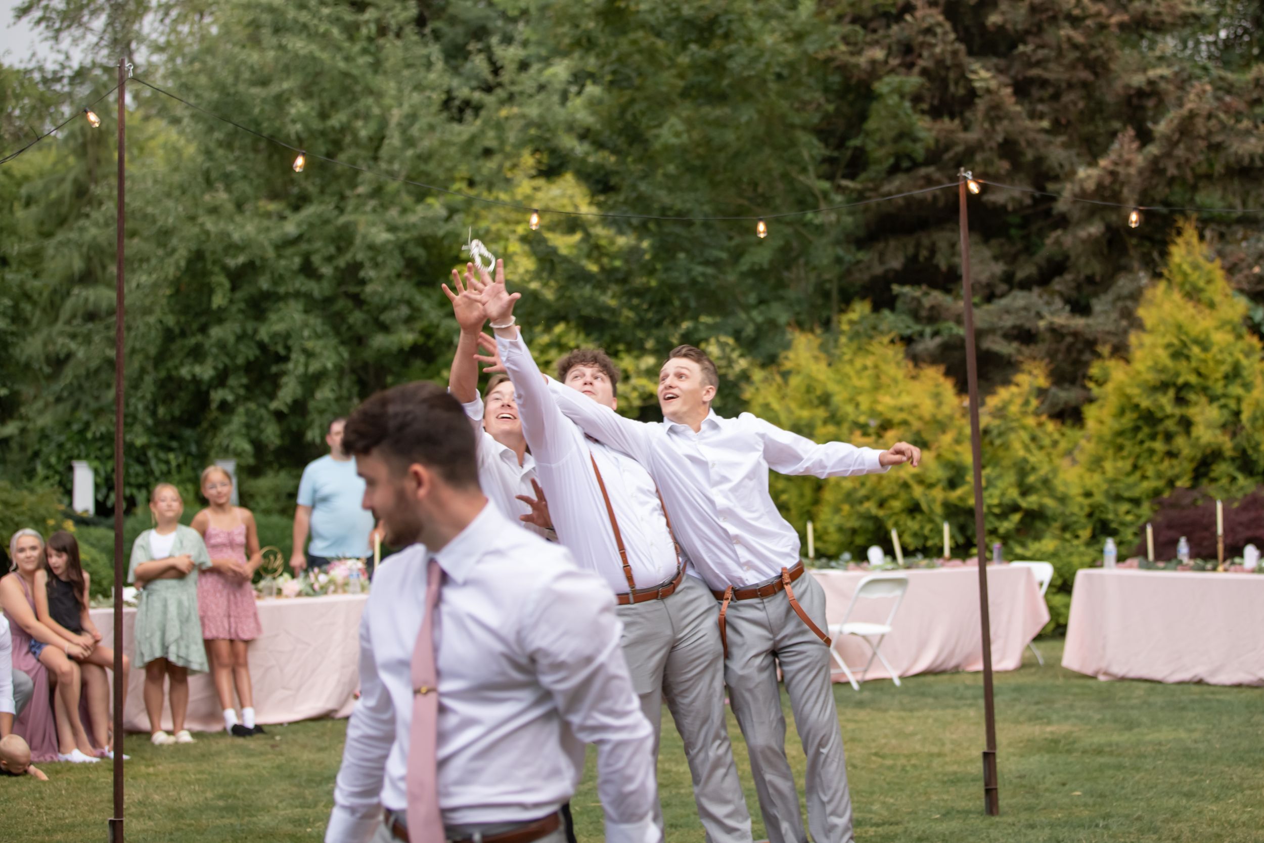 Celebration at an outdoor wedding reception as guests cheer and dance on the lawn.