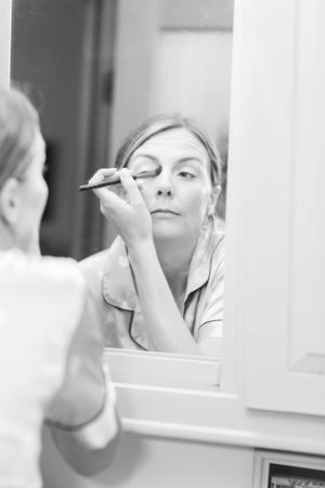 A woman applying eye makeup while looking in a mirror.