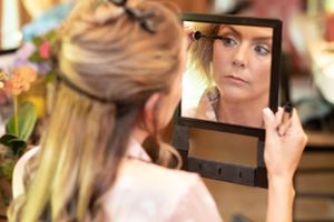 A woman applying makeup while looking in a handheld mirror.