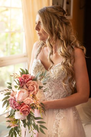 Dreamy wedding portrait showing intricate lace dress and romantic bouquet by sunlit window.