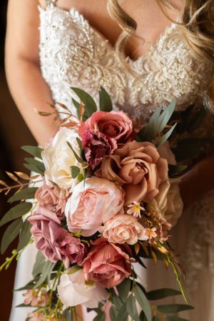 Elegant bridal bouquet featuring pink and mauve roses with eucalyptus leaves against a white lace wedding dress.