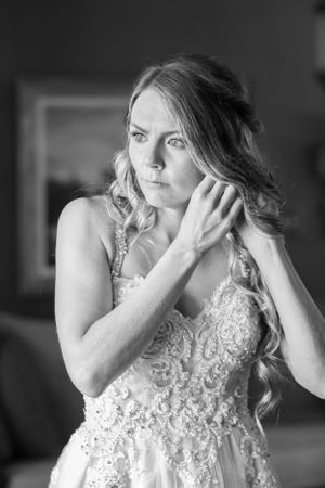 A woman in a white lace wedding dress touching her hair and looking to the side.