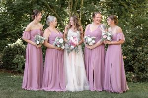 Bridal party in dusty rose dresses poses with bride in off-white gown holding bouquets.
