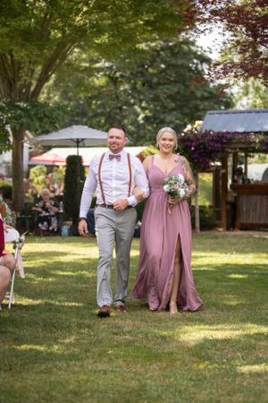 Wedding attendants walking down an outdoor aisle with pink decor and trees in the background.