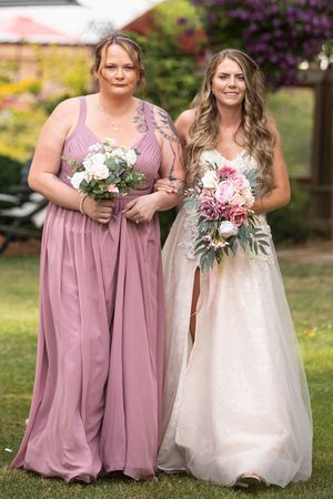 Bride in white gown and bridesmaid in mauve dress holding bouquets outdoors at a garden wedding ceremony.