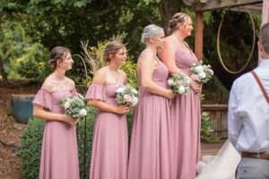 Row of bridesmaids in pink dresses holding bouquets during outdoor ceremony.
